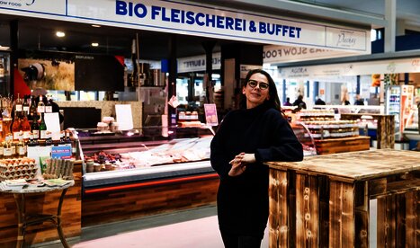 Eine Fleichereifachverkäuferin steht vor ihrem Geschäft, wo es biologische Produkte zu kaufen gibt.